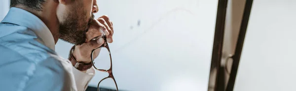 Tiro panorámico de comerciante bi-racial mirando a la computadora y sosteniendo gafas - foto de stock