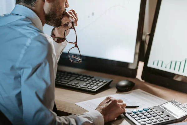 Ausgeschnittene Ansicht eines bi-rassischen Händlers, der auf den Computer blickt und eine Brille hält — Stockfoto