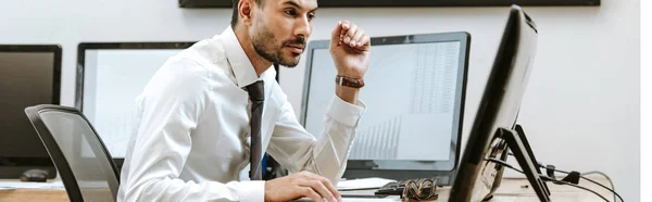 Panoramic shot of bi-racial trader looking at computer and sitting near computer with graphs — Stock Photo