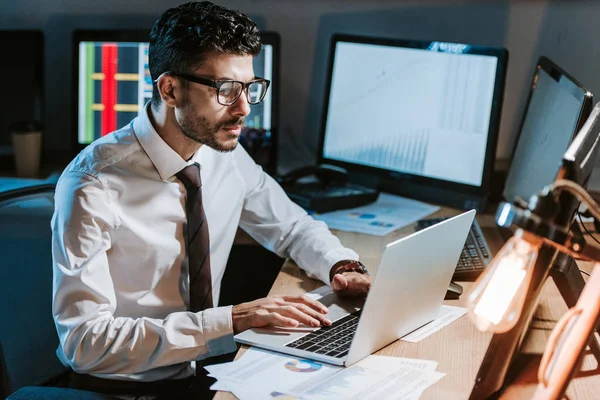 Trader bi-razziale utilizzando il computer portatile e seduto a tavola in ufficio — Foto stock