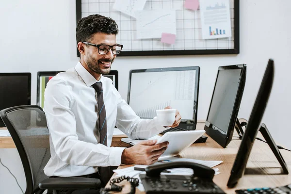 Smiling bi-racial trader using digital tablet and holding cup — Stock Photo