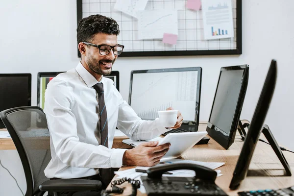 Comerciante bi-racial sonriente usando tableta digital y taza de celebración - foto de stock