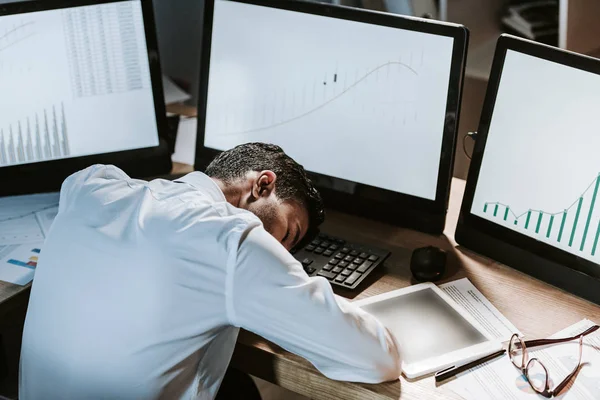 Visão de alto ângulo do comerciante bi-racial dormindo perto de computadores com gráficos — Fotografia de Stock