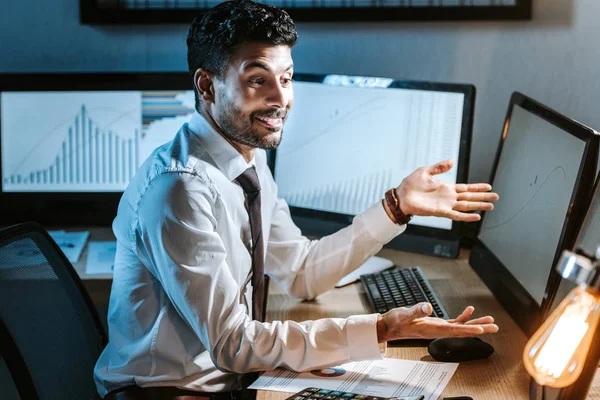 Lächelnder bi-rassischer Händler, der im Amt auf Computer mit Grafiken blickt — Stock Photo