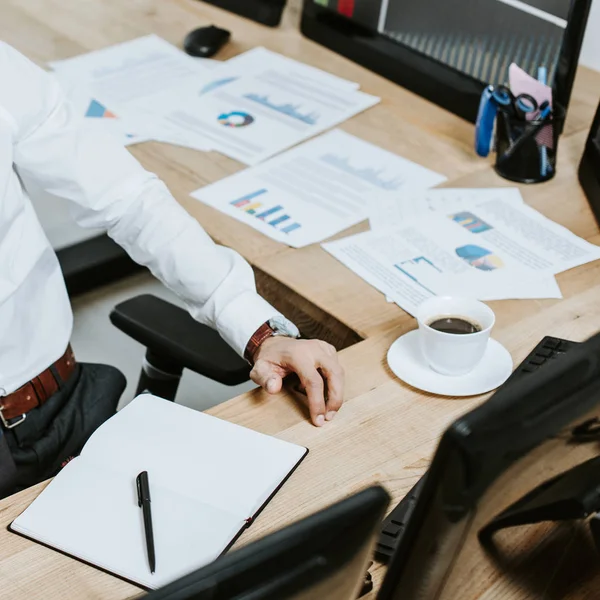 Cropped view of bi-racial trader sitting at table with papers — Stock Photo