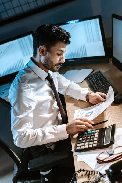 High angle view of bi-racial trader looking at paper and sitting at table — Stock Photo