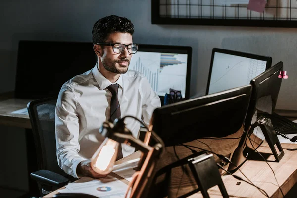 Bi-racial trader sitting at table and looking at computer — Stock Photo