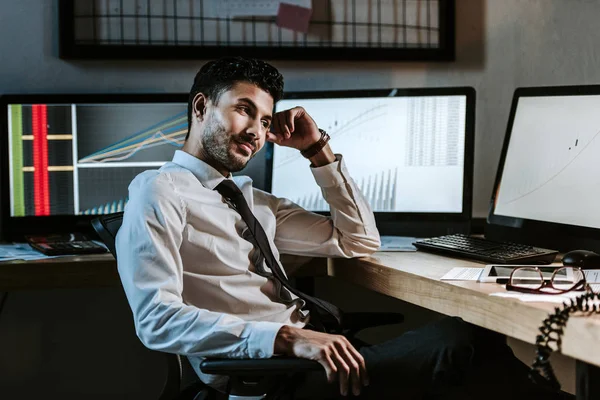 Lächelnder Händler zwischen den Rassen, der mit Grafiken im Büro neben Computern sitzt — Stock Photo