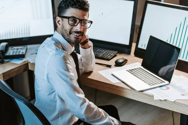 Vue grand angle du commerçant bi-racial souriant assis à table et regardant la caméra — Photo de stock