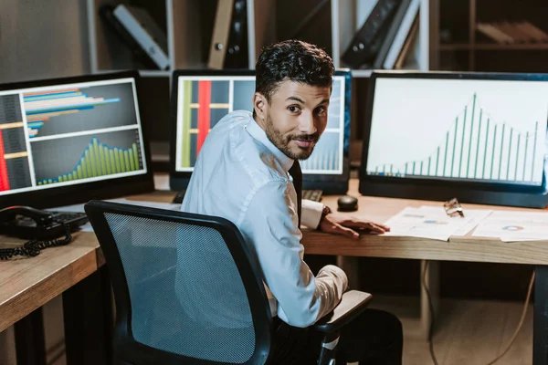 Souriant bi-racial trader assis près de la table et regardant la caméra — Photo de stock