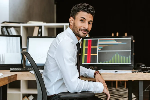 Smiling bi-racial trader sitting and looking at camera in office — Stock Photo