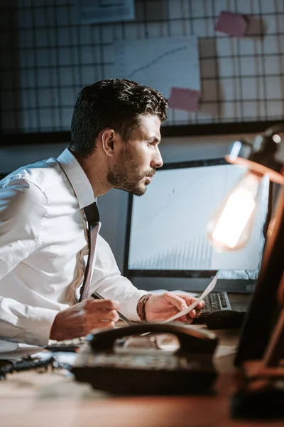 Seitenansicht eines gutaussehenden bi-rassischen Händlers, der Computer benutzt und am Tisch sitzt — Stockfoto