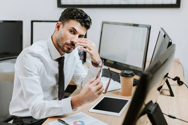 Bi-racial trader holding glasses and looking at camera in office — Stock Photo