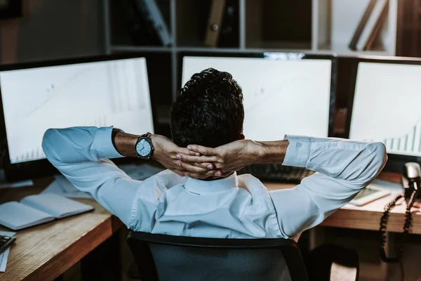 Back view of bi-racial trader with crossed arms looking at computers — Stock Photo