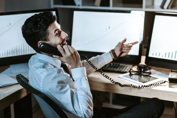 Lächelnder Händler zwischen den Rassen, der am Telefon spricht und am Tisch sitzt — Stockfoto