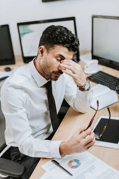 Vista ad alto angolo di stanco commerciante bi-razziale che tiene gli occhiali — Foto stock