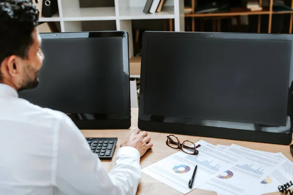 Selektiver Fokus eines Händlers zwischen Rassen, der mit Computern am Tisch sitzt — Stockfoto