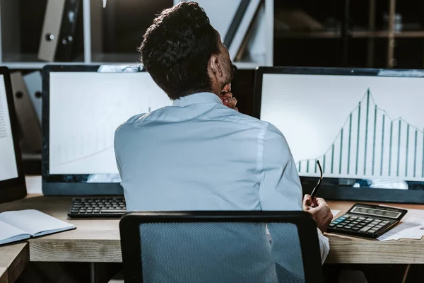 Back view of bi-racial trader sitting near computers with graphs — Stock Photo