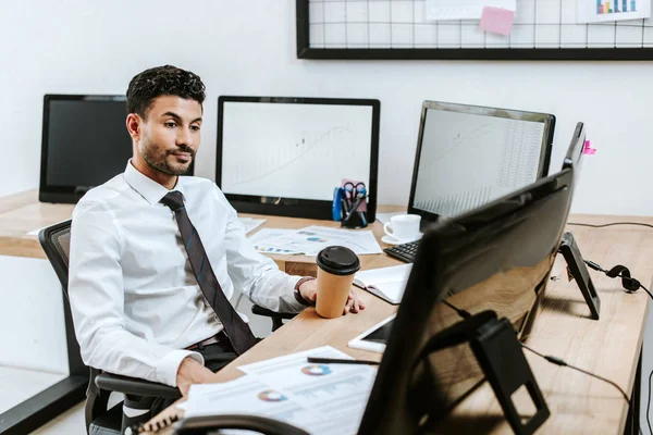 Bi-racial trader looking at computer and holding paper cup — Stock Photo