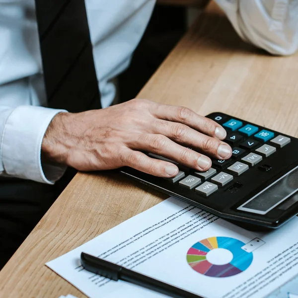 Cropped view of bi-racial trader using calculator and sitting at table — Stock Photo
