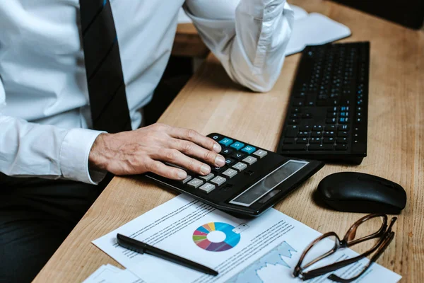 Vista recortada del comerciante bi-racial utilizando la calculadora y sentado a la mesa - foto de stock