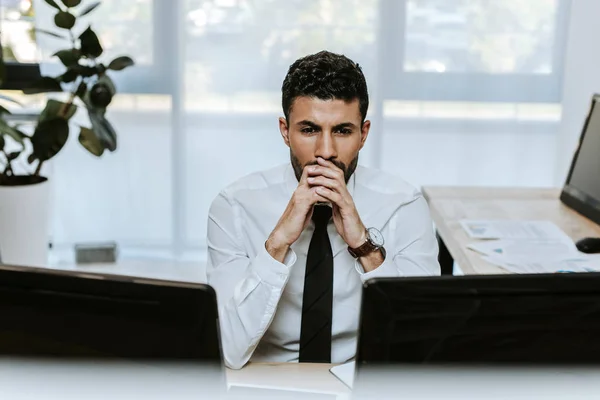 Pensativo y guapo bi-racial comerciante mirando a la computadora en la oficina - foto de stock