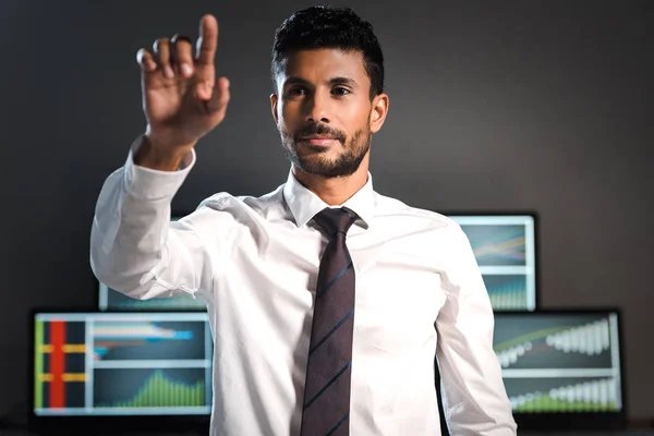 Selective focus of bi-racial trader pointing with finger and computers on background — Stock Photo