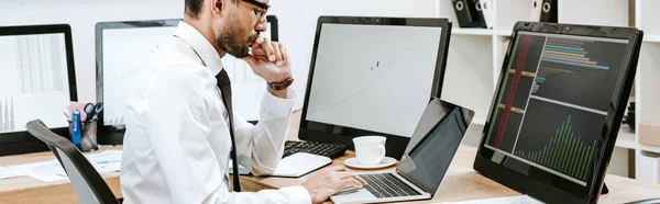 Panoramic shot of bi-racial trader using laptop and sitting at table — Stock Photo