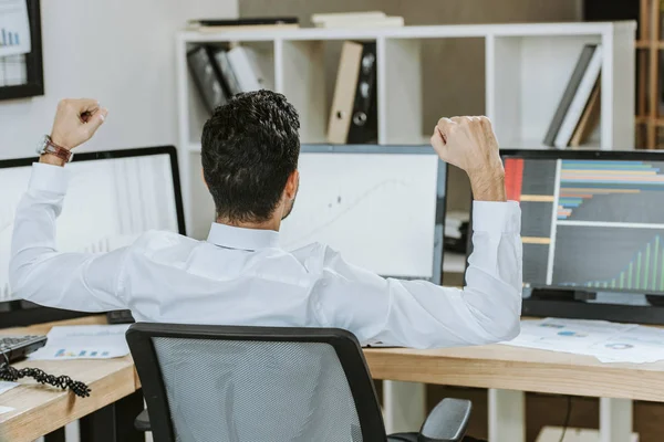 Rückansicht eines bi-rassischen Händlers, der Ja-Geste zeigt und neben Computern mit Grafiken sitzt — Stockfoto