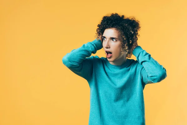 Adolescent frisé effrayé avec bouche ouverte regardant loin isolé sur jaune — Photo de stock