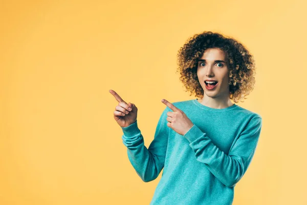 Curly teenager with open mouth pointing with fingers aside isolated on yellow — Stock Photo