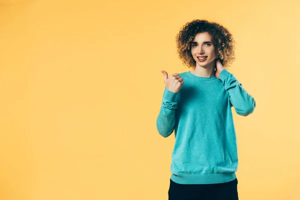 Smiling curly teenager showing thumb up isolated on yellow — Stock Photo