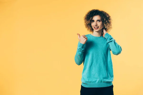 Sonriente rizado adolescente mostrando pulgar hacia arriba aislado en amarillo - foto de stock