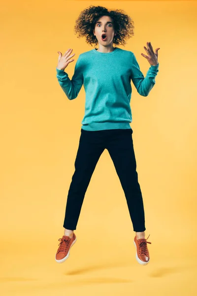 Шокований кучерявий підліток стрибає на жовтому — стокове фото