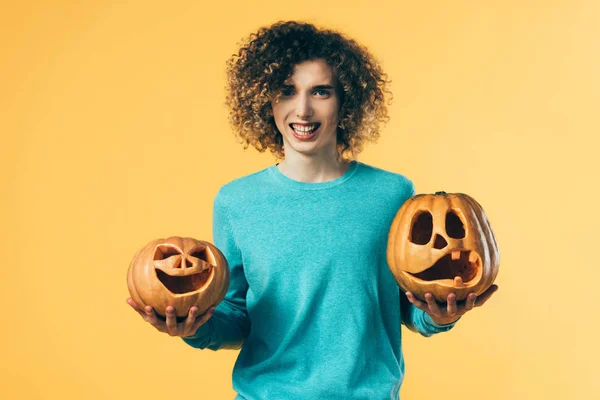 Rizado adolescente celebración de Halloween calabazas aislado en amarillo - foto de stock