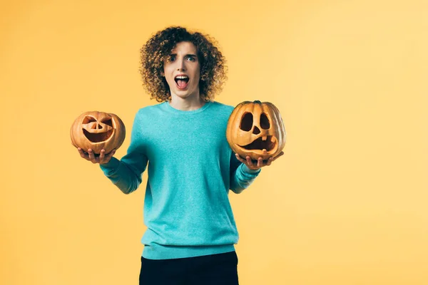 Scared curly teenager holding Halloween pumpkins and screaming isolated on yellow — Stock Photo