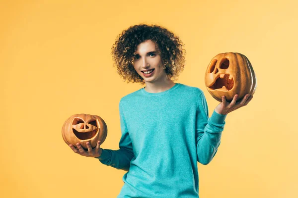 Sonriente rizado adolescente celebración de Halloween calabazas aislado en amarillo - foto de stock