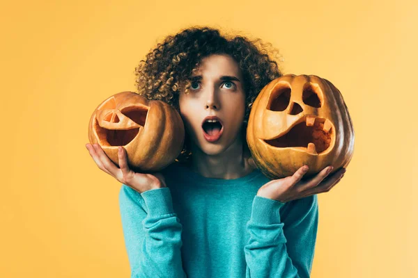 Scared curly teenager holding Halloween pumpkins isolated on yellow — Stock Photo