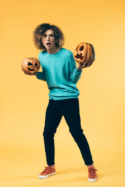 Scared curly teenager holding Halloween pumpkins on yellow — Stock Photo