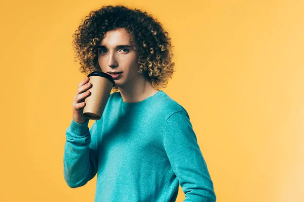 Curly teenager drinking coffee from paper cup isolated on yellow — Stock Photo