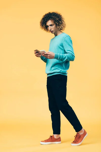 Curly teenager holding smartphone and credit card on yellow — Stock Photo