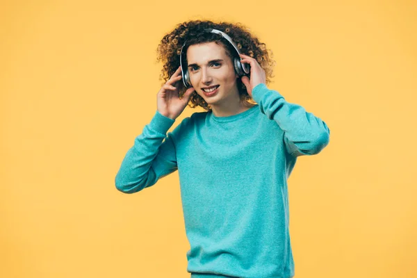 Улыбающийся кудрявый подросток слушает музыку в наушниках, изолированных на желтый — стоковое фото