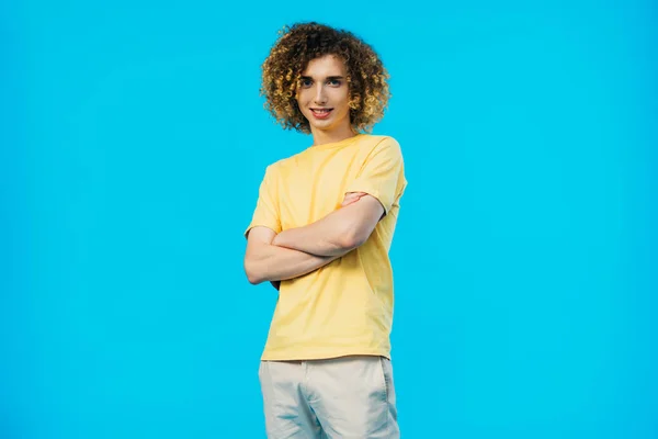 Sorrindo encaracolado adolescente com braços cruzados isolado em azul — Fotografia de Stock