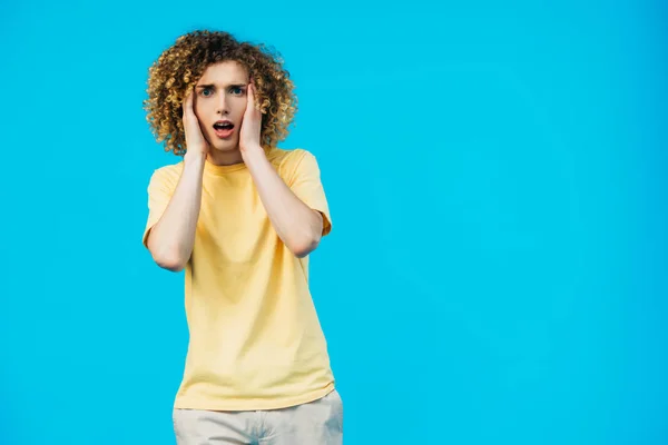Scared curly teenager with hands on head isolated on blue — Stock Photo