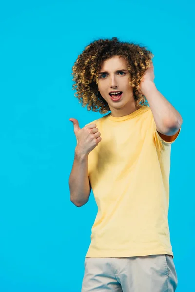 Adolescent bouclé montrant pouce vers le haut et toucher les cheveux isolés sur bleu — Photo de stock