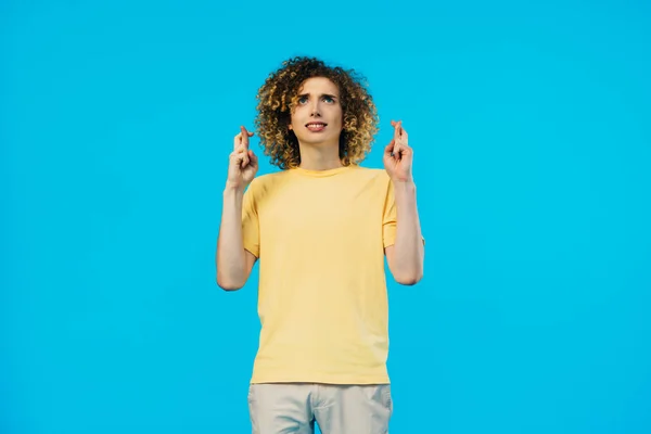 Worried curly teenager with crossed fingers isolated on blue — Stock Photo