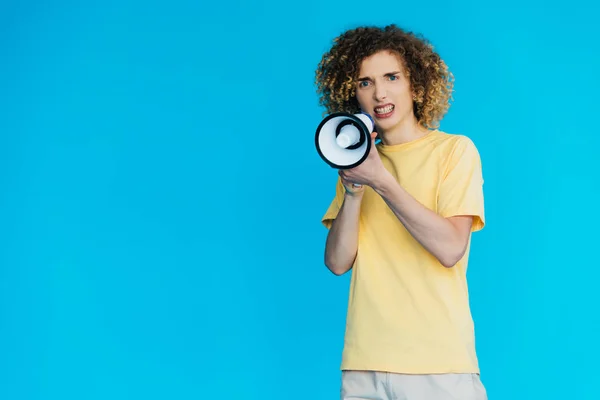 Angry curly teenager screaming in loudspeaker isolated on blue — Stock Photo