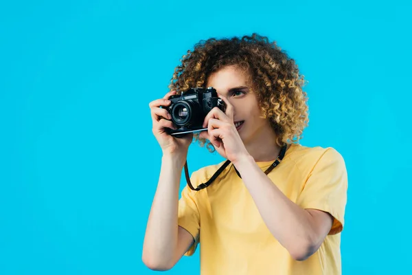 Rizado adolescente tomando foto en película cámara aislado en azul - foto de stock