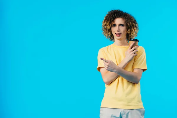 Curly teenager with coffee to go pointing with finger aside isolated on blue — Stock Photo