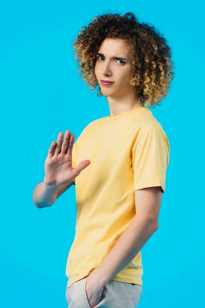 Роздратований фігурний підліток з рукою в кишені показує стоп жест ізольований на синьому — стокове фото